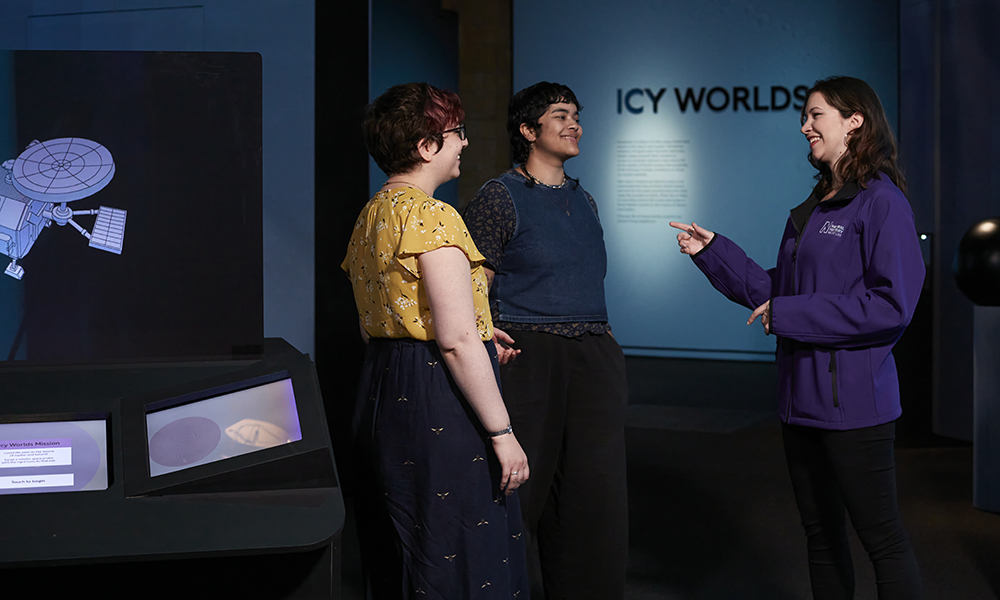 A tour guide talks to two people at the Space exhibition in front of a sign that reads Icy Worlds