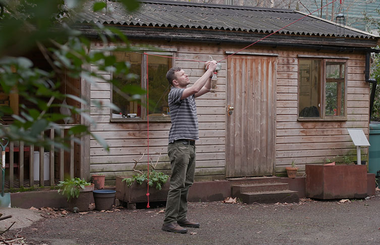 Joe hangs up a new plastic bottle bird feeder in the Museum's garden