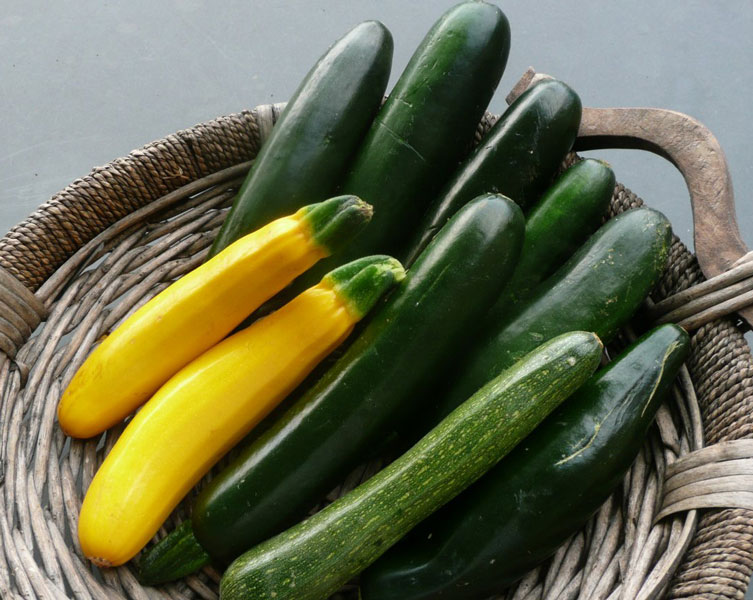 Green and yellow zuchinnis in a straw basket