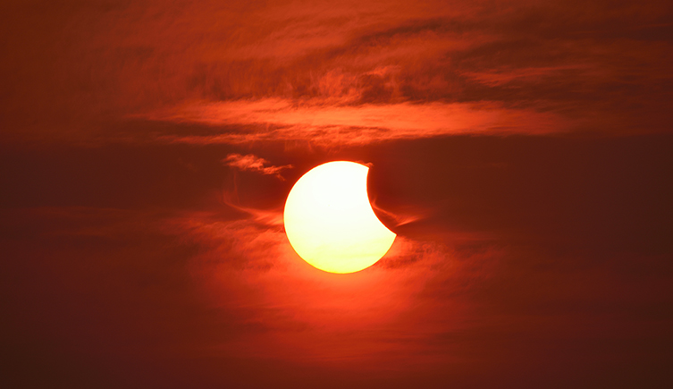A partial solar eclipse, which looks a bit like a bite has been taken out of the yellow Sun
