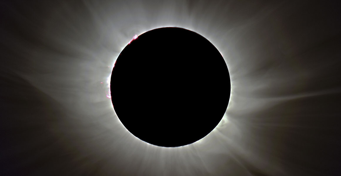 Black and white photo showing a black disc surrounded by streams of wispy light